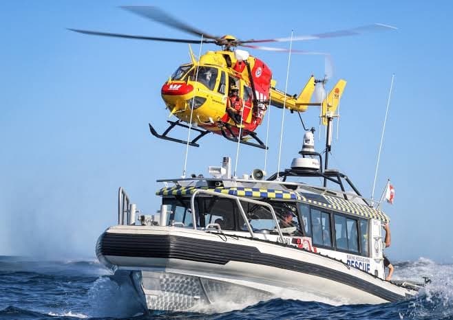 A marine rescue vessel at sea working with a rescue helicopter overhead.
